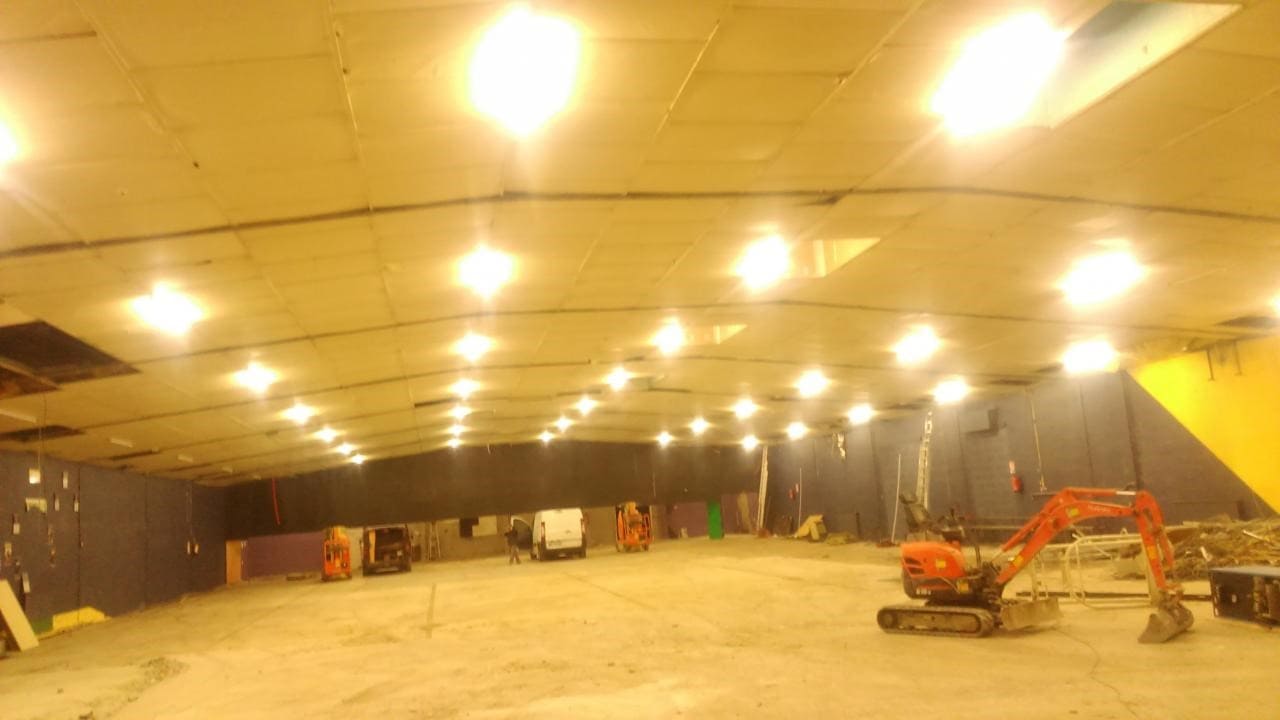 Photo d'un hangar avec 35 systèmes d'éclairage au plafond, une mini pelle mécanique, deux voitures de type utilitaire et deux chariots élévateurs sont stationnés à l'intérieur. 