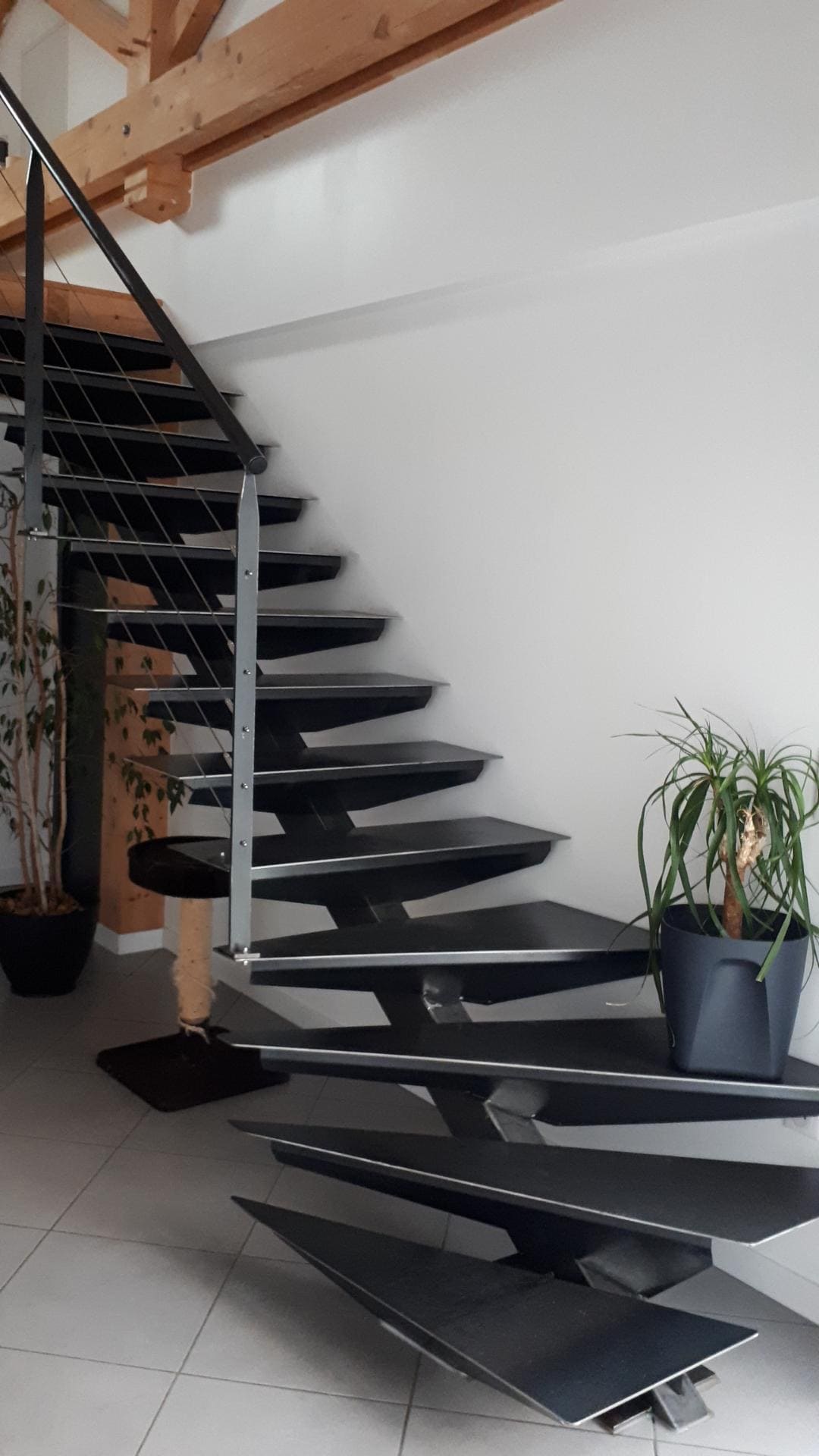 Photo d'un escalier d'angle et suspendu en fer noir devant un mur blanc.