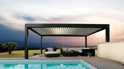 Photo d'une pergola en fer noir devant une piscine, les poteaux sont carrés et le toit est en lattes orientables, un salon d'extérieur est disposé en dessous.