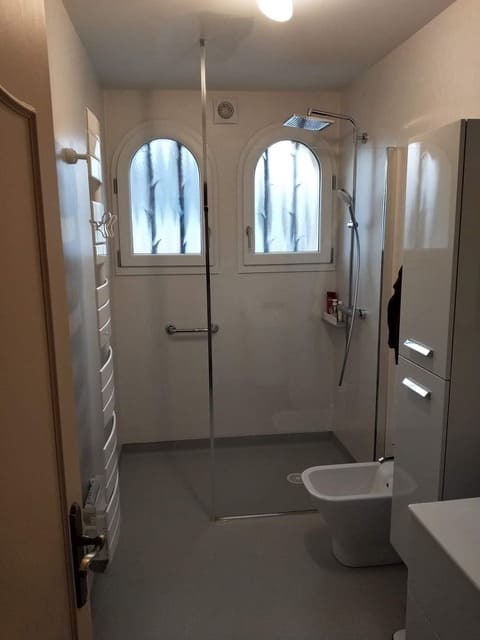 Photo d'une salle de bain aux murs blanc une sol gris et une douche a l'italienne vitrée avec une poignée pour les personnes a mobilité réduite.